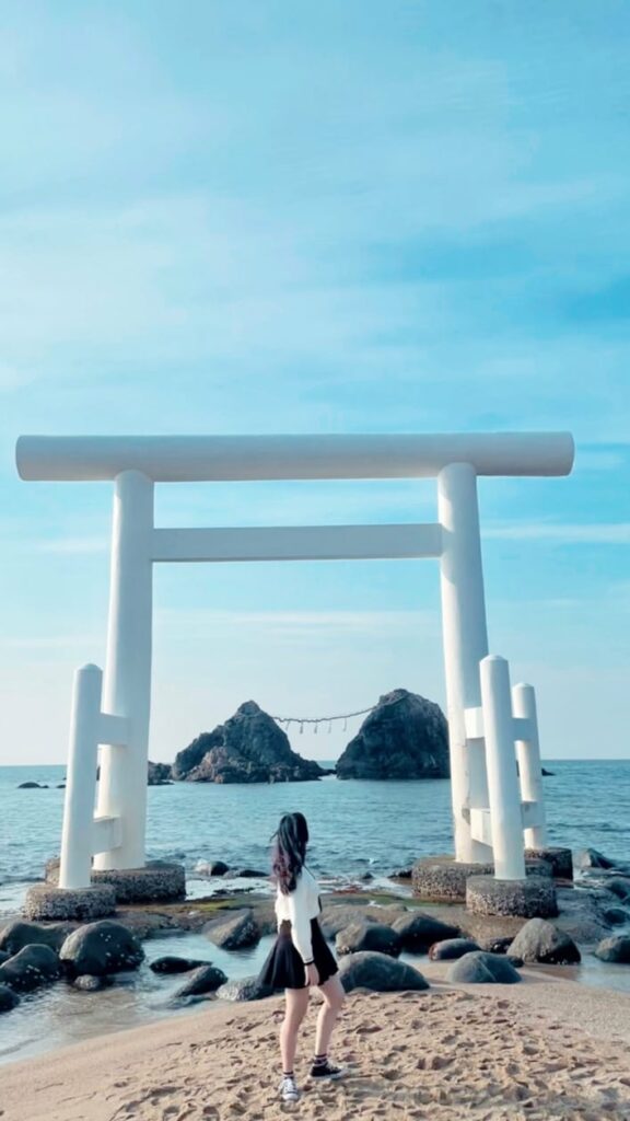 A woman standing on the beach next to a tori tori gate.