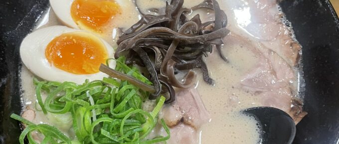 Bowl of tonkotsu ramen with sliced pork, boiled eggs, green onions, and black mushrooms, served in a black bowl.