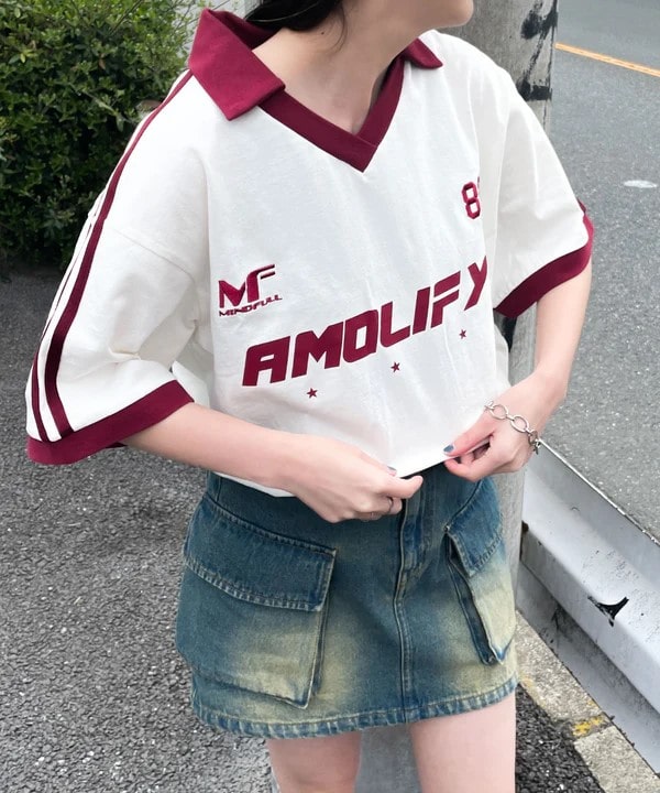 Person standing outdoors wearing a white and maroon "AMOLIFY" jersey, and a denim skirt with large pockets.