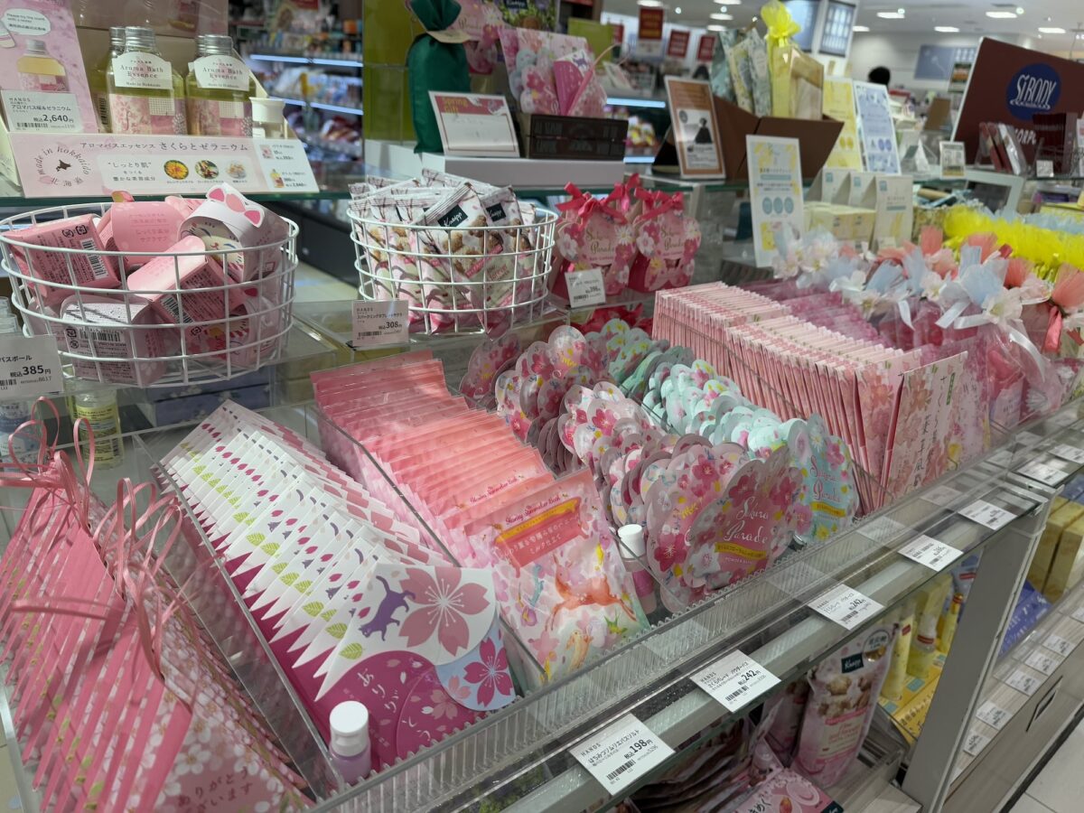 A store display showcasing an array of pink-themed packaged goods, including gift bags, bath salts, and more, all neatly organized on shelves. Some items feature limited edition cherry blossom designs inspired by the beauty of Japan.