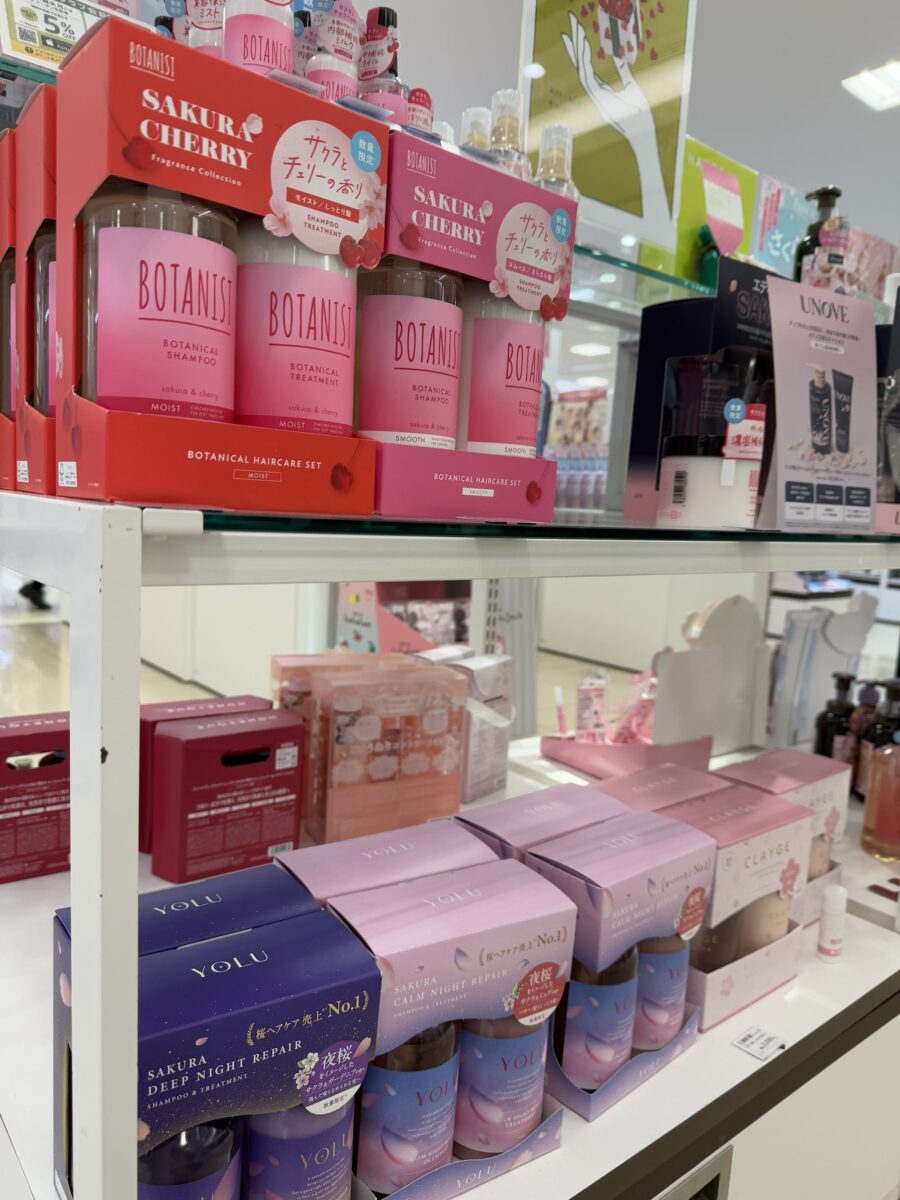 The store display features shelves of pink-themed hair and skincare products, including Botanis and Yolu brands, reminiscent of Cherry Blossom Goods.