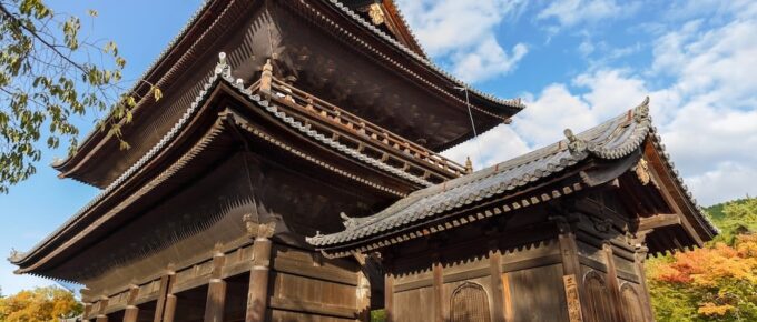 A large traditional wooden Japanese temple surrounded by trees, under a partly cloudy sky.