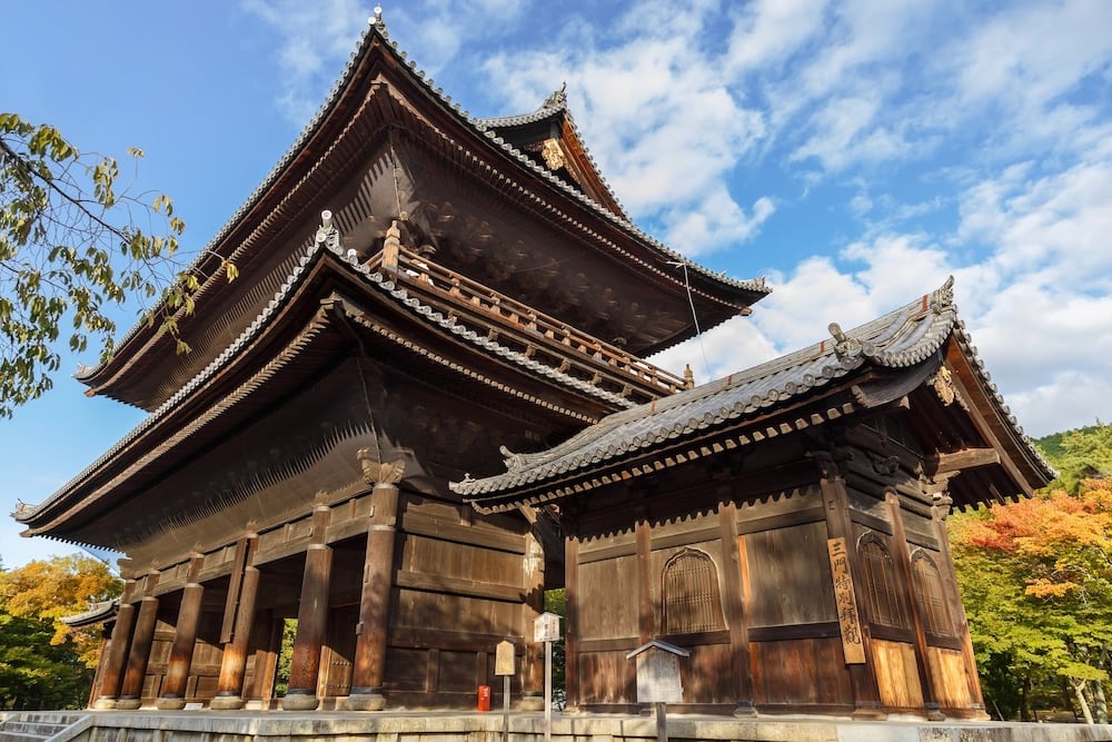 A large traditional wooden Japanese temple surrounded by trees, under a partly cloudy sky.